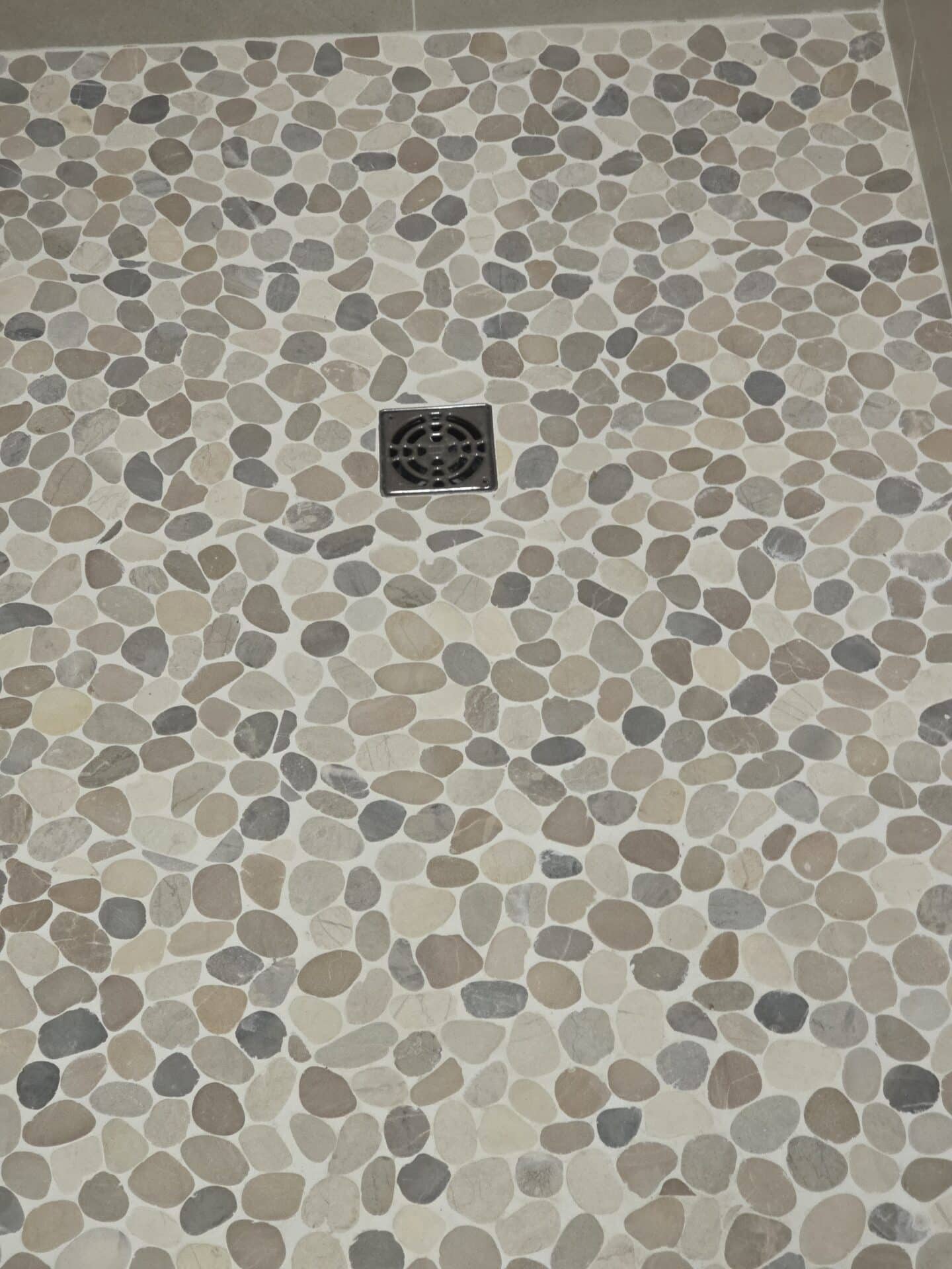 Pebble tile shower floor sloped to a centre drain on a waterproofed shower pan
