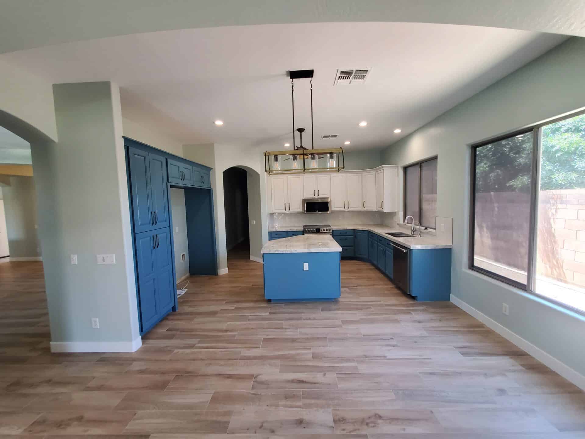 Open-plan kitchen and living space after a whole-home remodel, with blue cabinetry and wood-look tile flooring